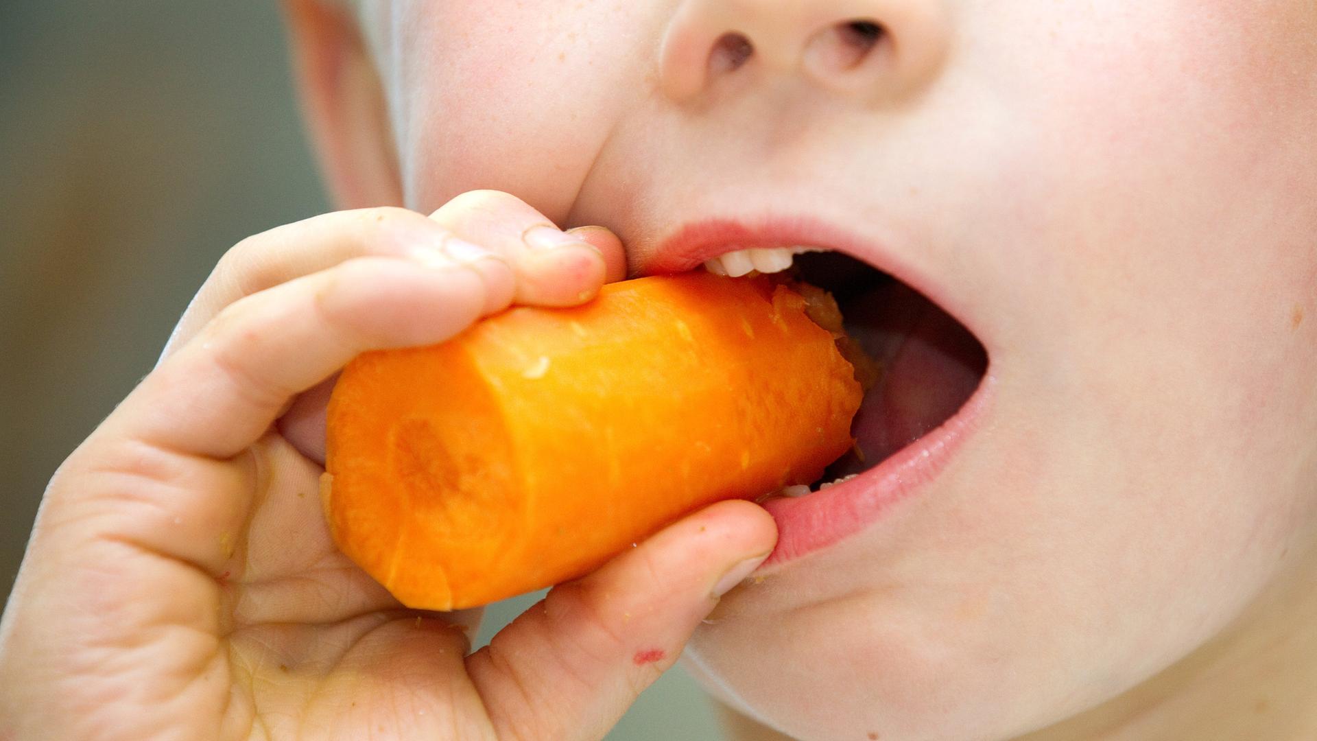 Kind beißt in eine Karotte