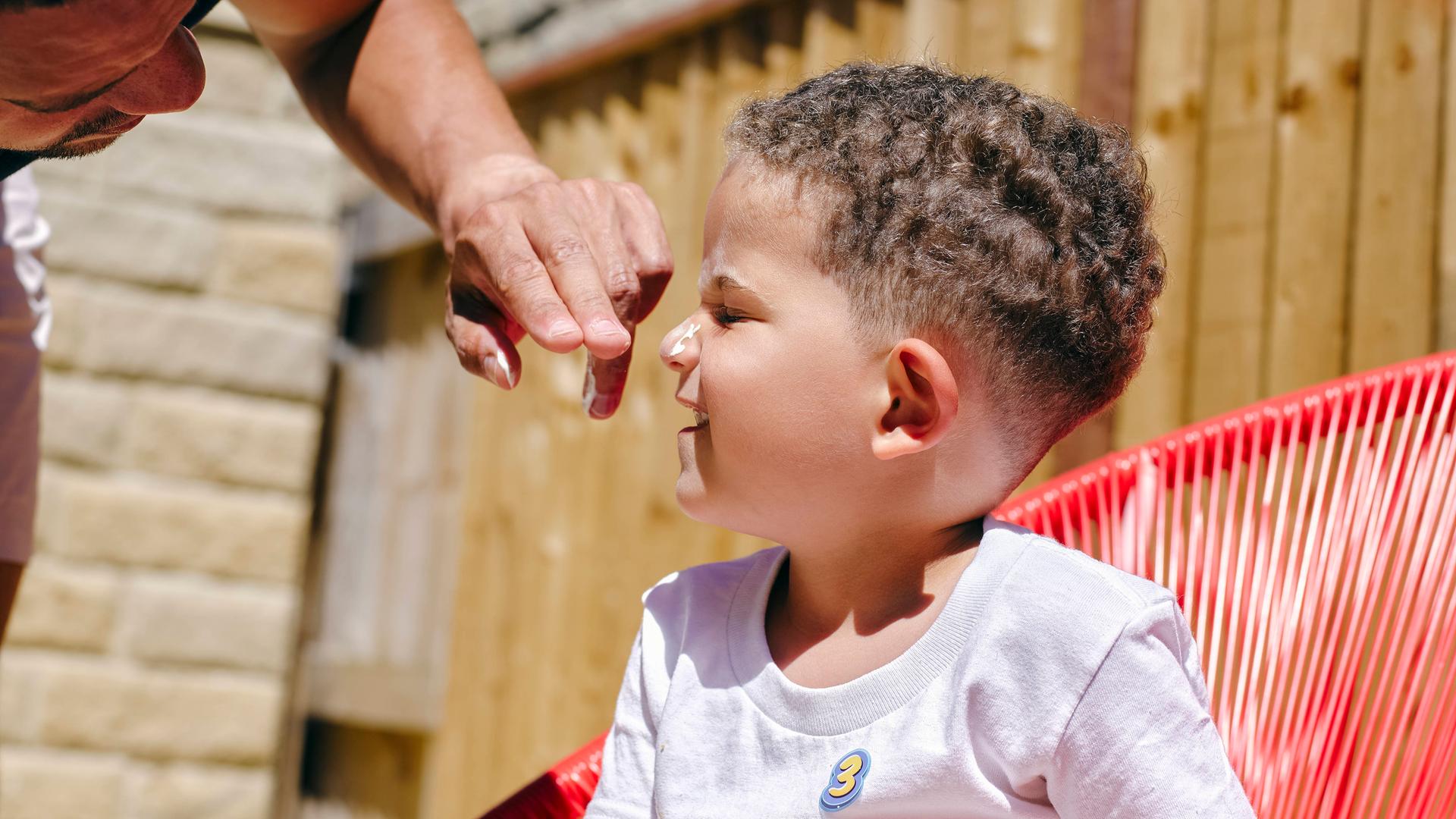 Ein Kind bekommt das Gesicht mit Sonnencreme eingecremt.