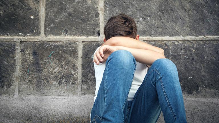 Ein Junge sitzt traurig an einer Wand. (Symbolbild)