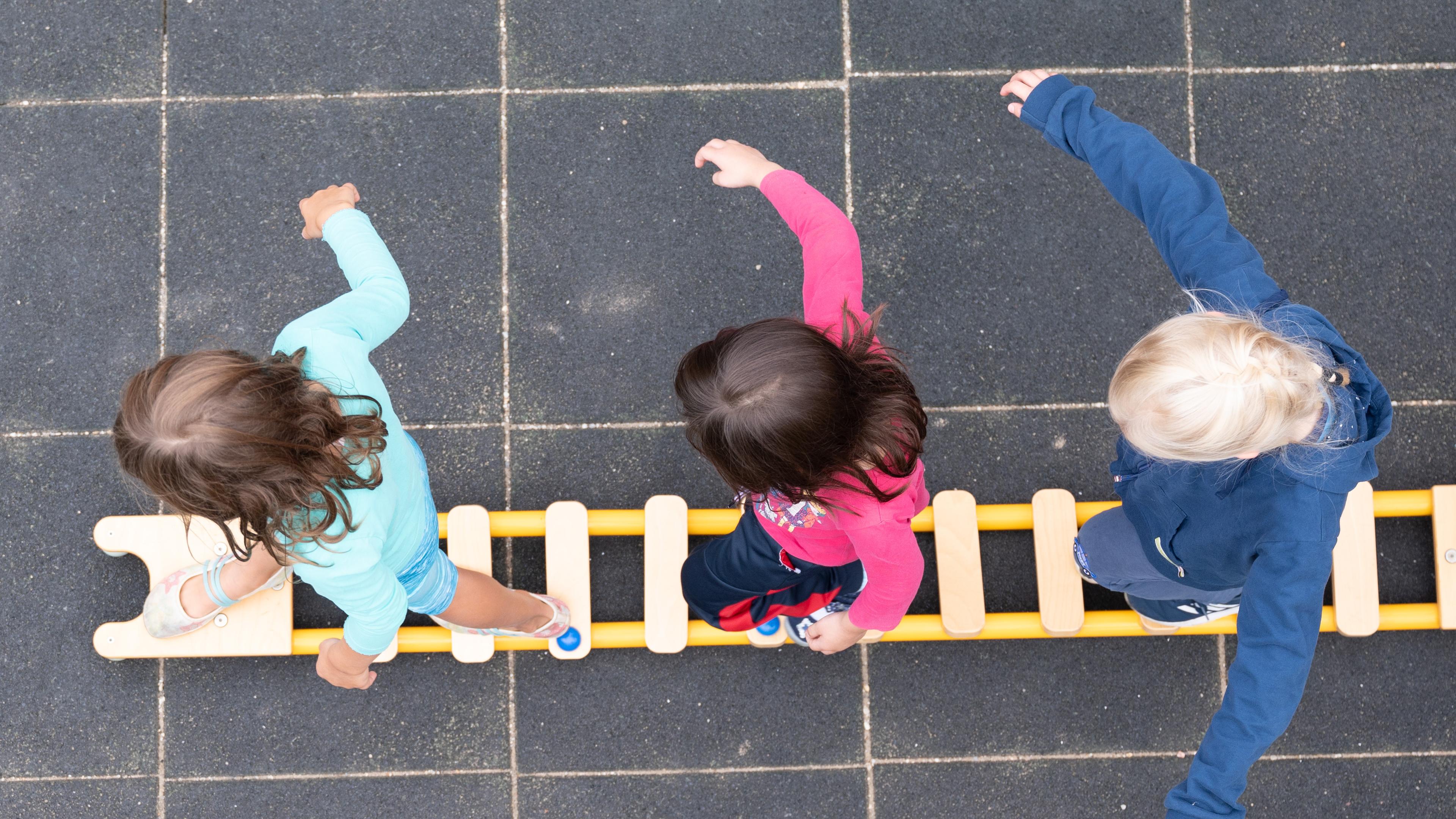 Drei Kinder balancieren auf einem Spielplatz