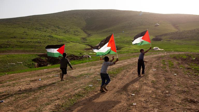 Kinder schwenken die palästinensische Fahne während sie durch ein Tal rennen