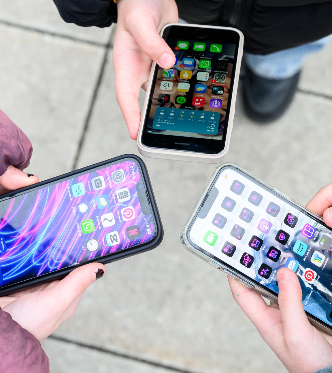 Drei junge Menschen im einem Kreis halten ihre entsperrten Smartphones gemeinsam in die Mitte. 