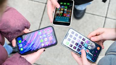 Drei junge Menschen im einem Kreis halten ihre entsperrten Smartphones gemeinsam in die Mitte. 