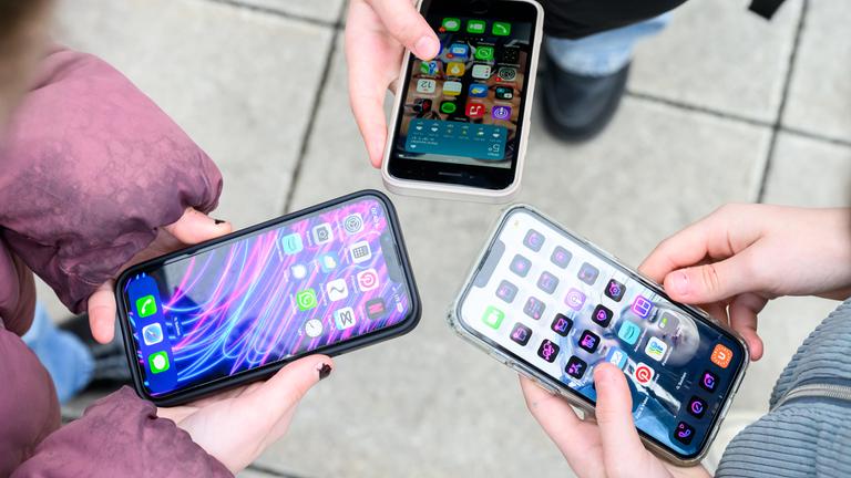 Drei junge Menschen im einem Kreis halten ihre entsperrten Smartphones gemeinsam in die Mitte. 