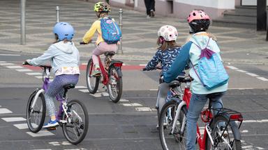 Vier Kinder fahren mit Fahrrädern hintereinander auf einer Straße.
