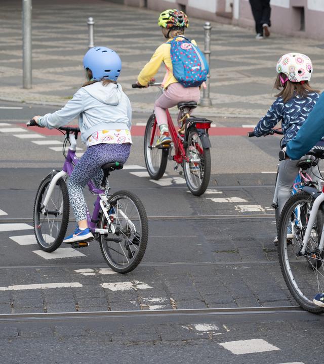 Vier Kinder fahren mit Fahrrädern hintereinander auf einer Straße.
