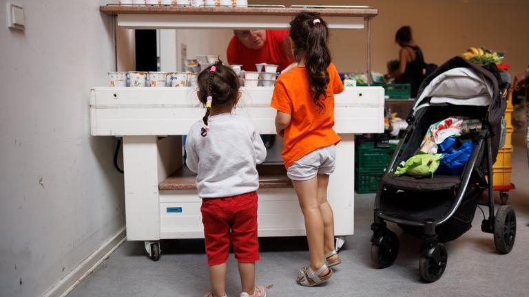 Ein Mitarbeiter verteilt Jogurt an zwei Kinder in der Ausgabestelle Paul-Schneider-Haus der Berliner Tafel. Kinder sind von hinten zu sehen.