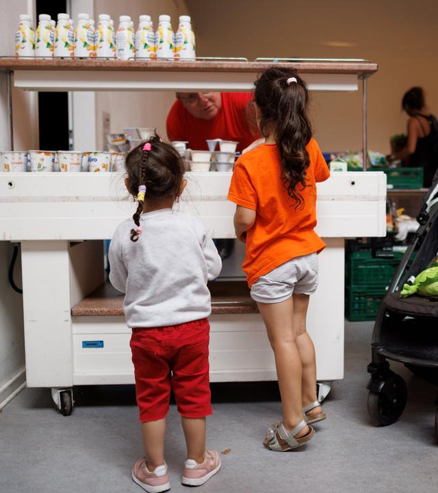 Ein Mitarbeiter verteilt Jogurt an zwei Kinder in der Ausgabestelle Paul-Schneider-Haus der Berliner Tafel. 
