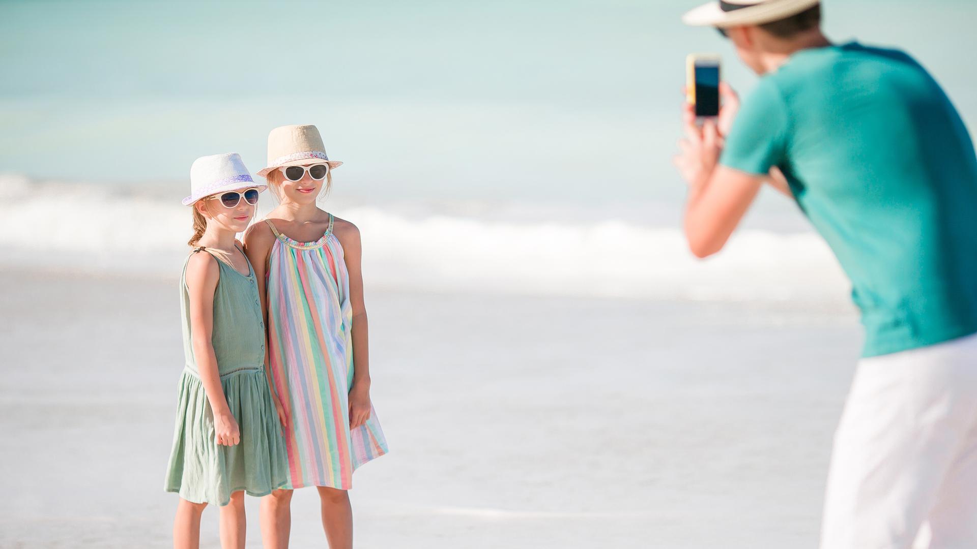 Mann fotografiert seine Kinder am Strand.