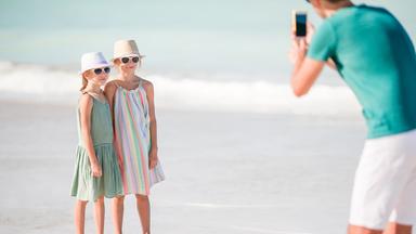 Mann fotografiert seine Kinder am Strand.