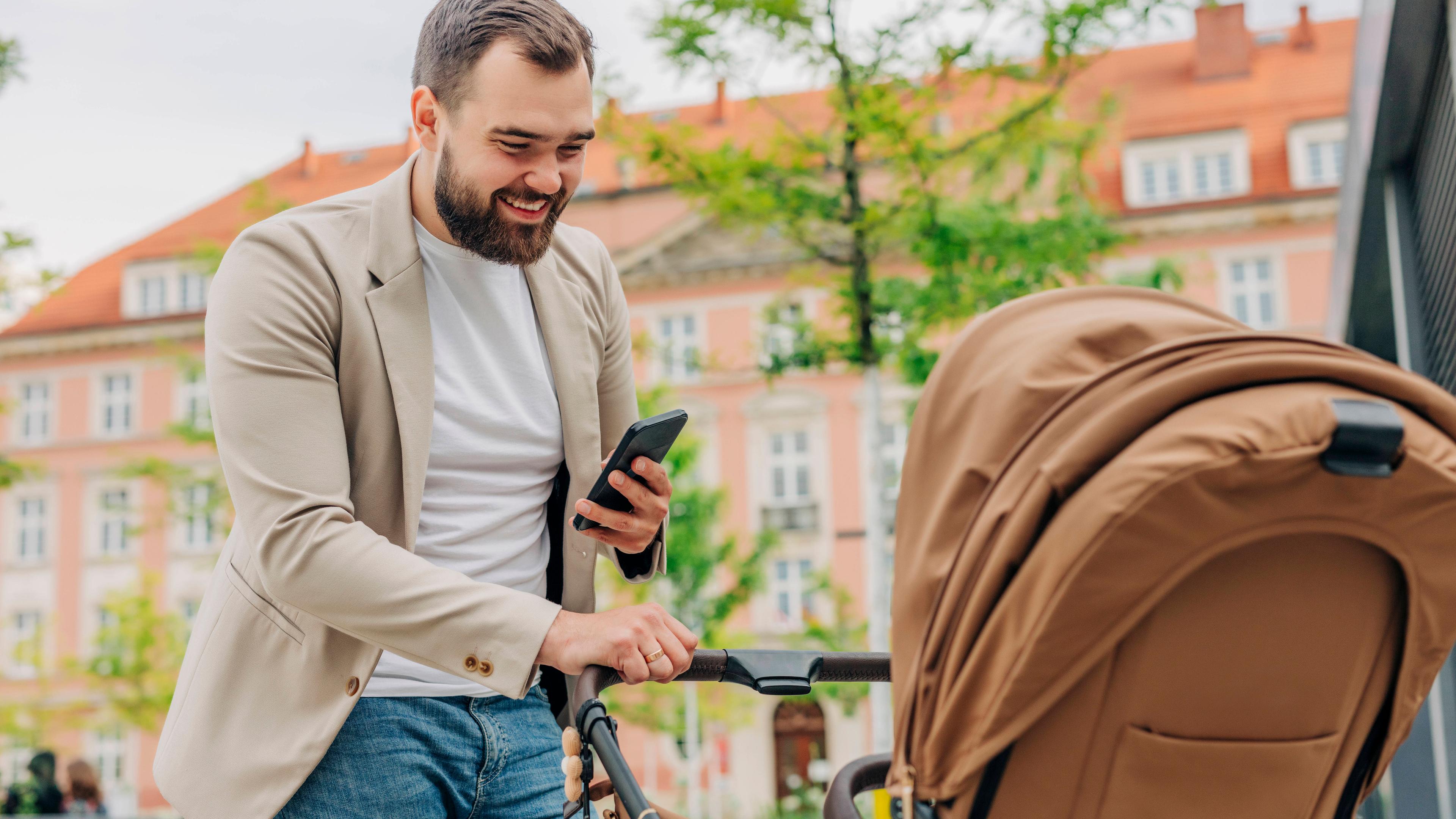 Mann mit Handy blickt in Kinderwagen