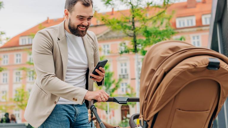 Mann mit Handy blickt in Kinderwagen