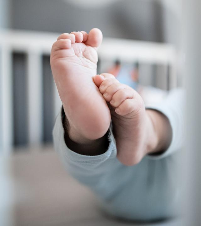 Die Füße eines Babys sind in einem Kinderbett zu sehen.