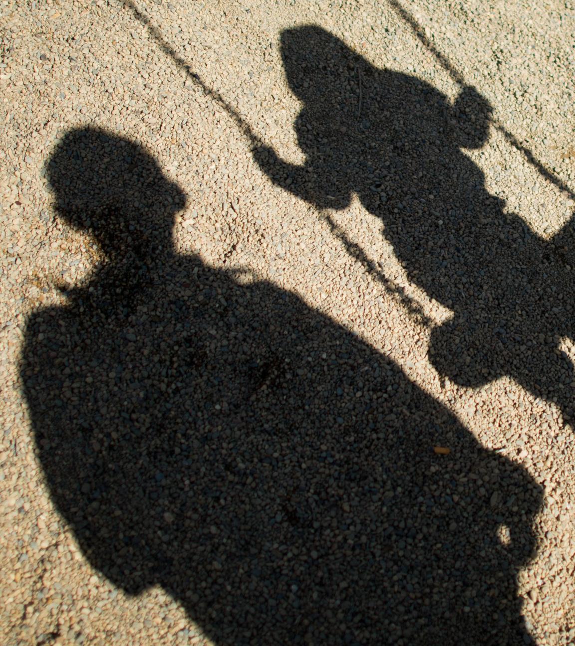 Schatten eines Kindes auf einer Schaukel und eines Erwachsenen daneben