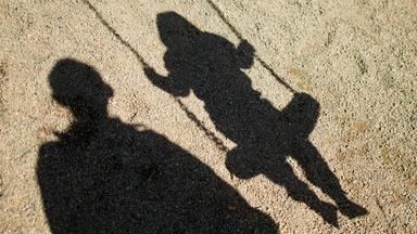 Schatten eines Kindes auf einer Schaukel und eines Erwachsenen daneben