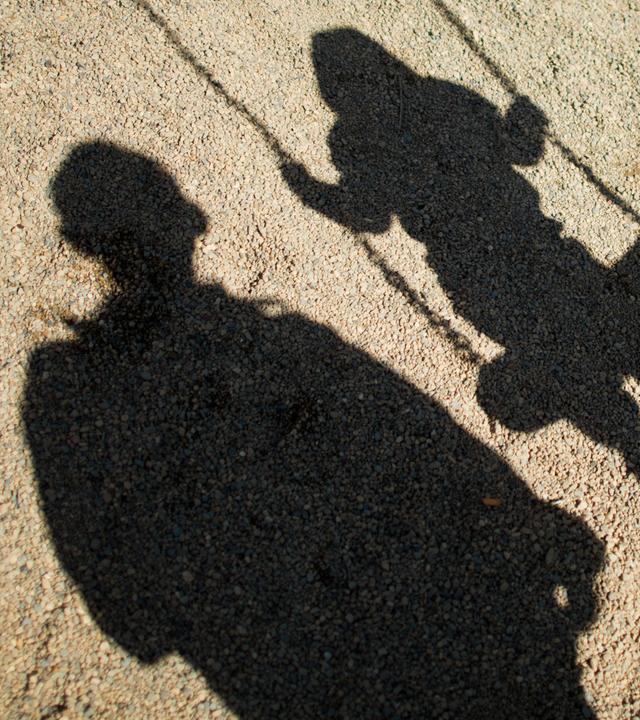 Schatten eines Kindes auf einer Schaukel und eines Erwachsenen daneben