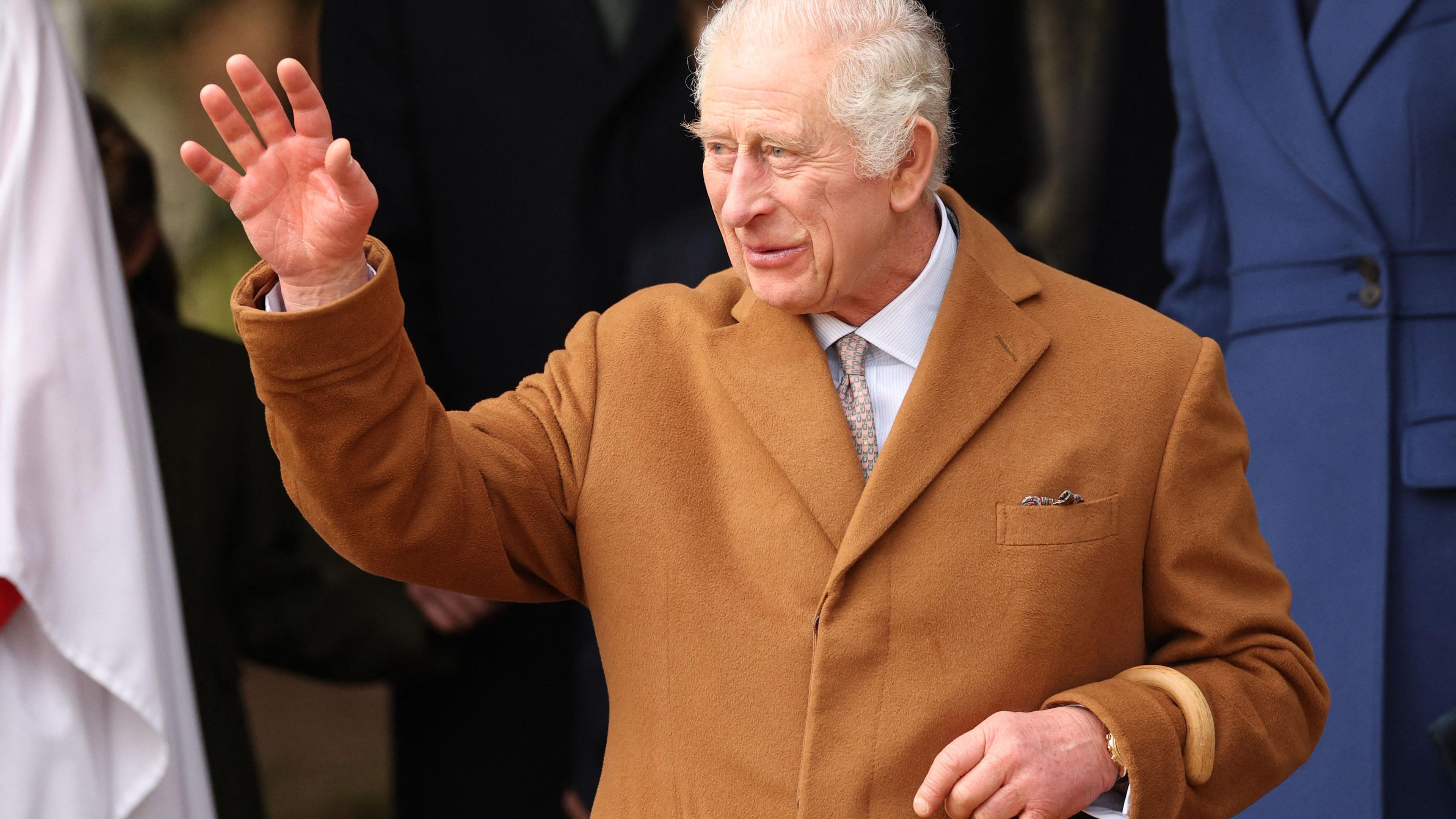 König Charles steht im Freien und winkt zu umstehenden Personen