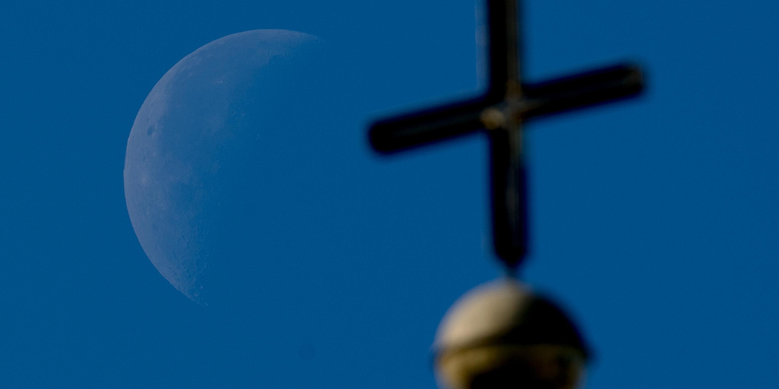 Symbolbild: Der abnehmende Viertelmond ist in Kassel hinter einem Kirchenkreuz der St.-Elisabeth-Kirche zu sehen. 