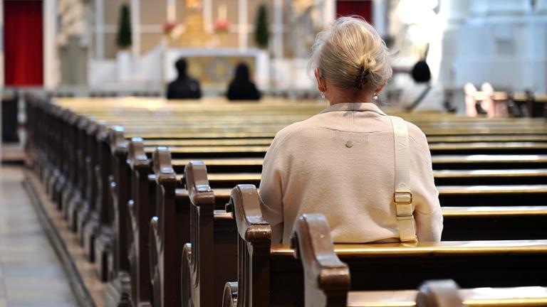 In einer fast leeren Kirche sitzt nur eine ältere Person auf der Kirchbank.