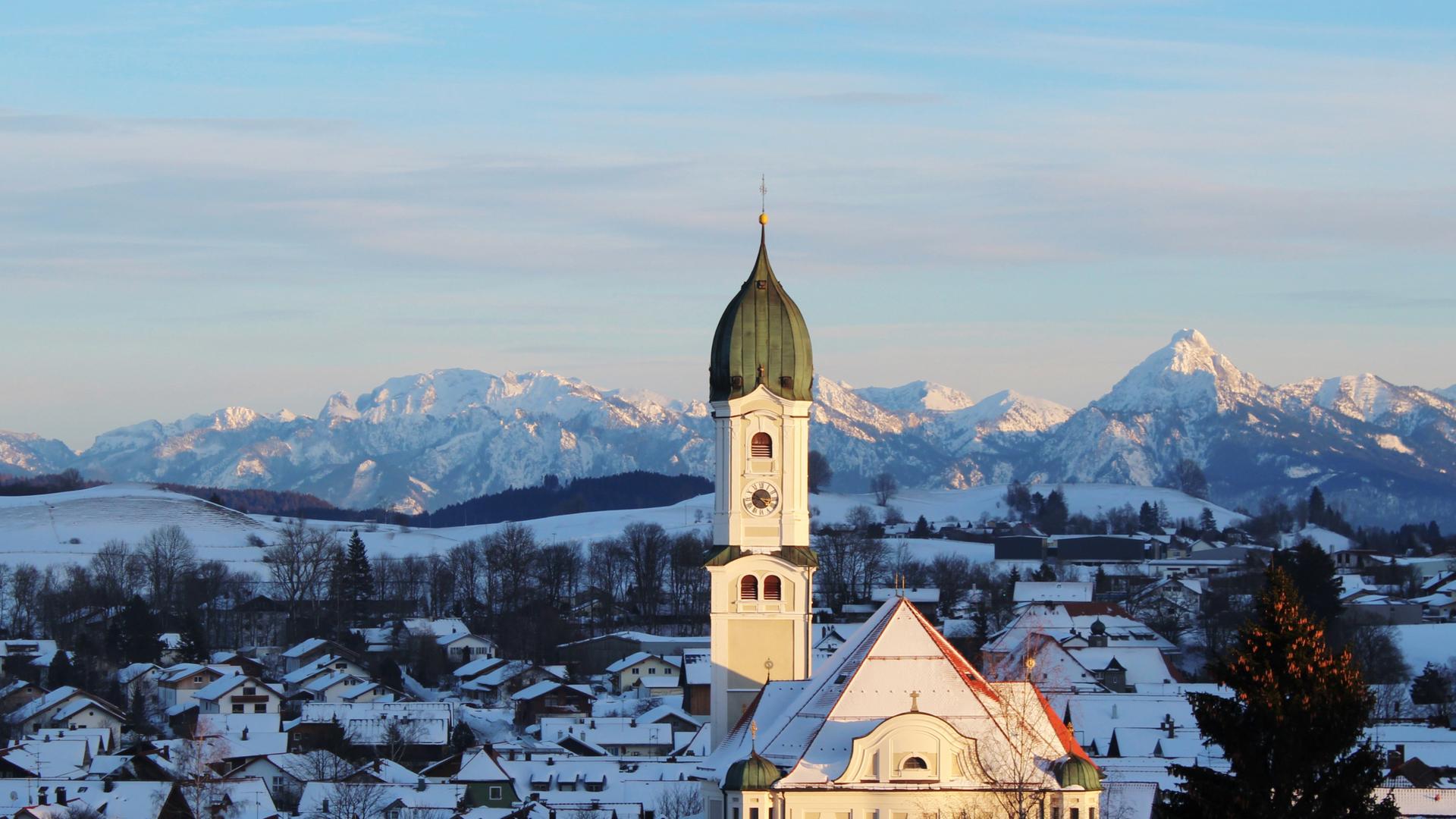 Ein Kirchturm vor einem Berg-Panorama.