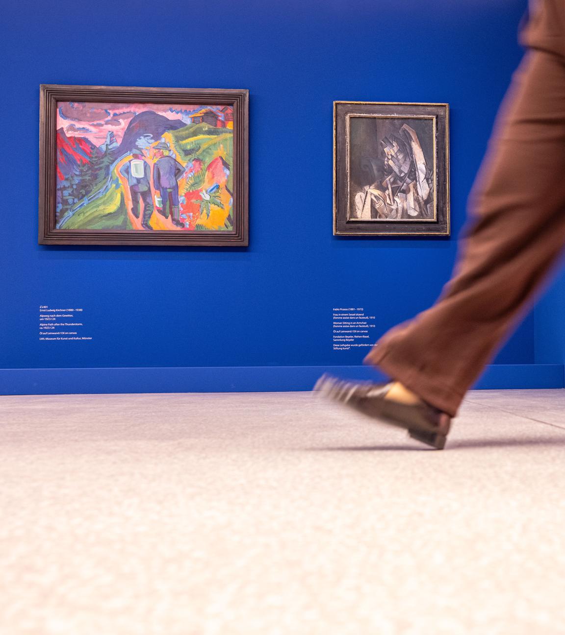 23.09.2025, Nordrhein-Westfalen, Münster: Im LWL Museum für Kunst und Kultur geht eine Frau vor einem Gemälde von Ernst Ludwig Kirchner und einem Gemälde von Pablo Picasso.