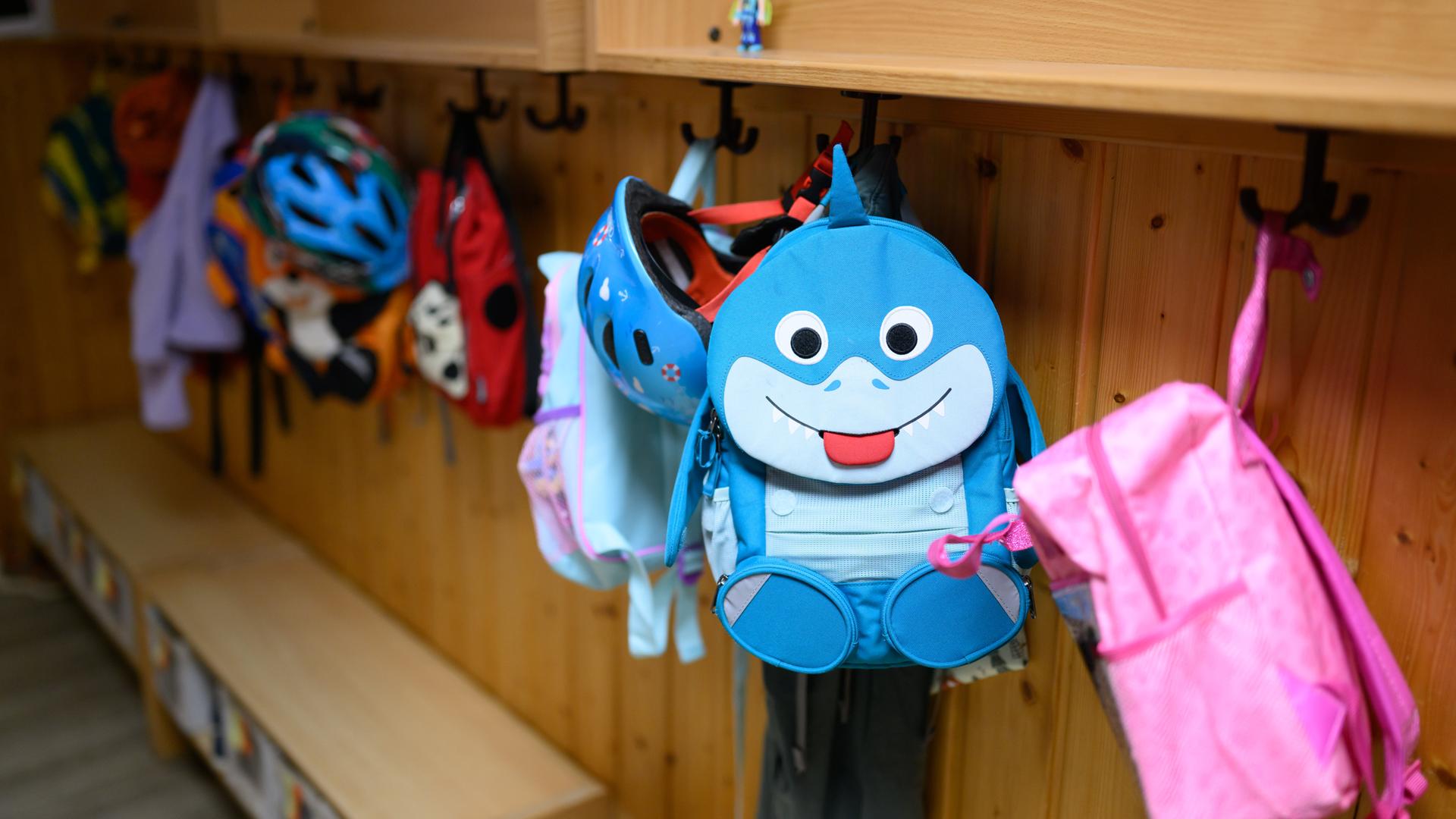 Bunte Kinderrucksäcke hängen an einer Gaderobe.