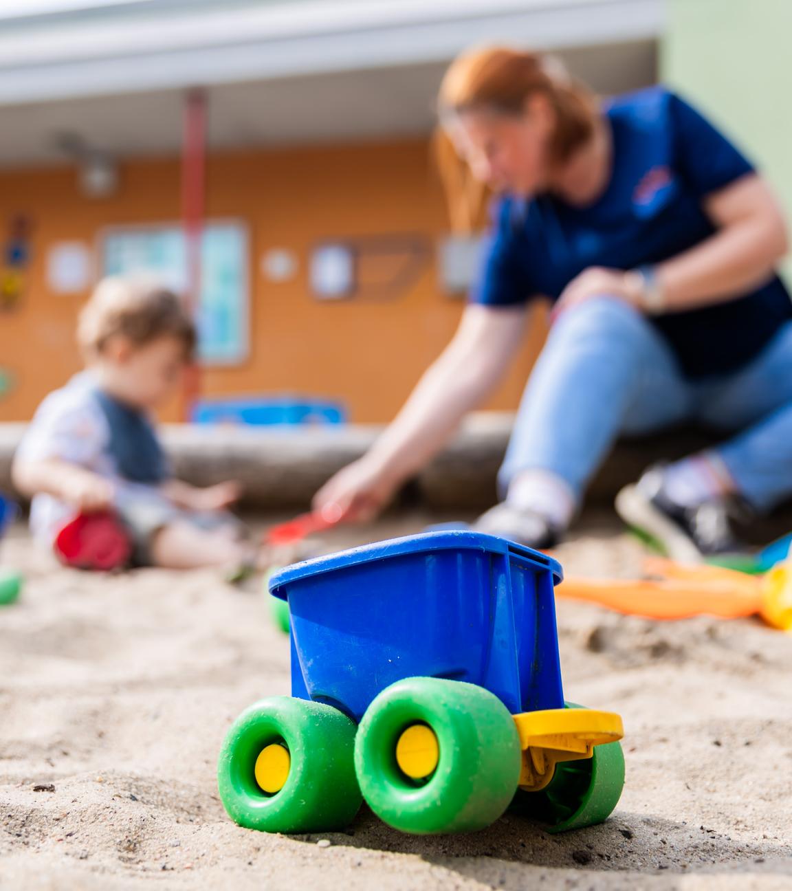 Ein Kind spielt mit einer Erzieherin im Sandkasten einer Kita.