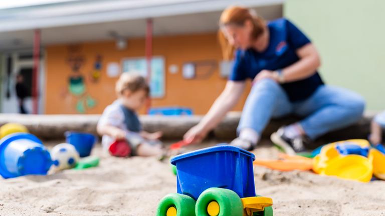 Ein Kind spielt mit einer Erzieherin im Sandkasten einer Kita.