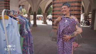 Frau hält sich eine Kittelschürze an den Körper, die gerade ein Modetrend ist.