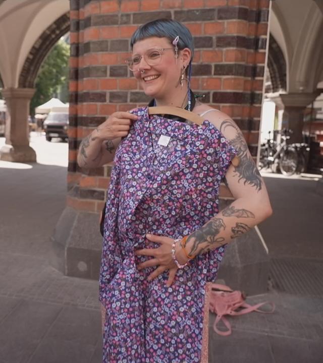 Frau hält sich eine Kittelschürze an den Körper, die gerade ein Modetrend ist.