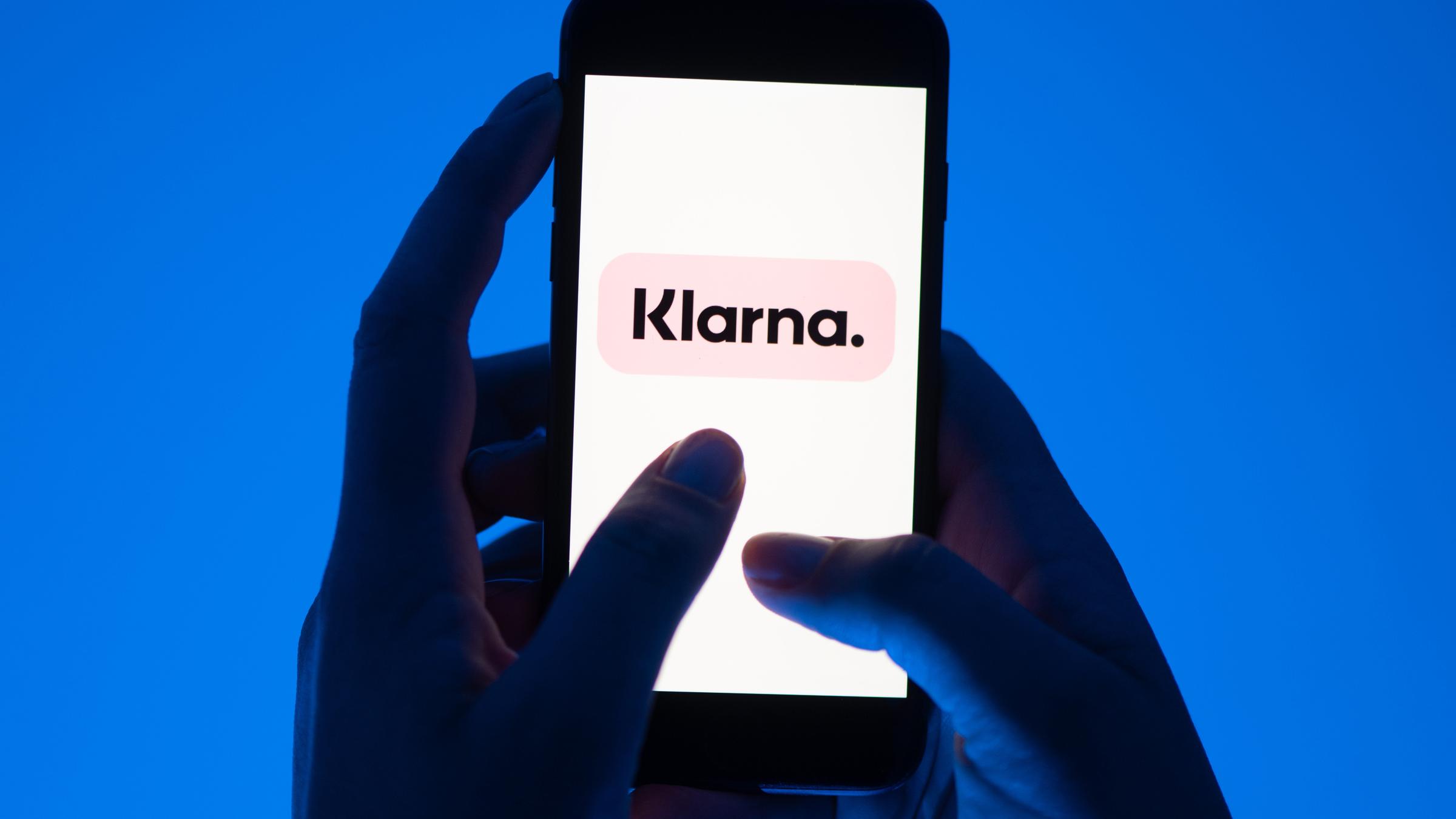 Das Logo der Firma Klarna ist auf einem Smartphone zu sehen, das von einer Person gehalten wird.