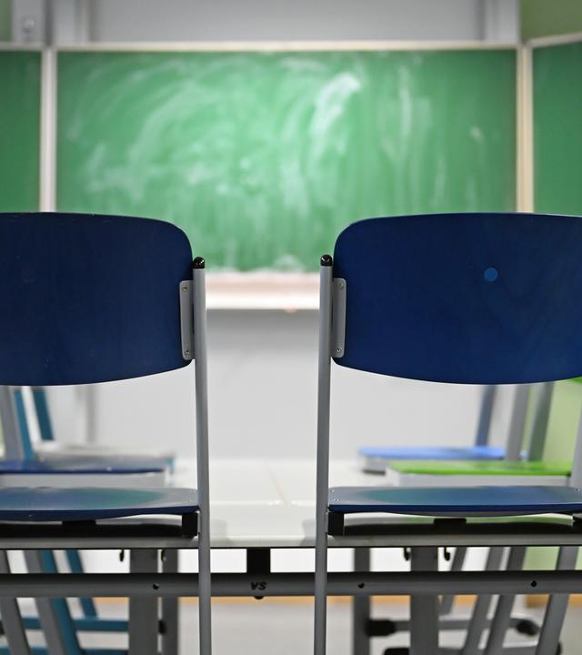 Zwei leere Stühle stehen in einem Klassenraum vor einer Tafel. (Symbolbild)