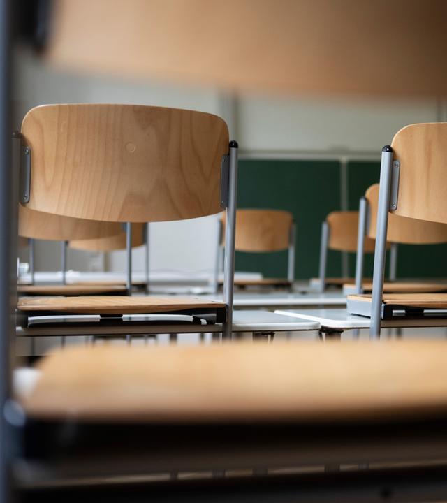 Stühle und eine Tafel sind in einem Schulraum zu sehen.
