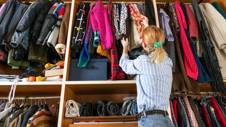 Ein Frau steht vor einem übervollen Kleiderschrank und wählt Kleidung aus. 