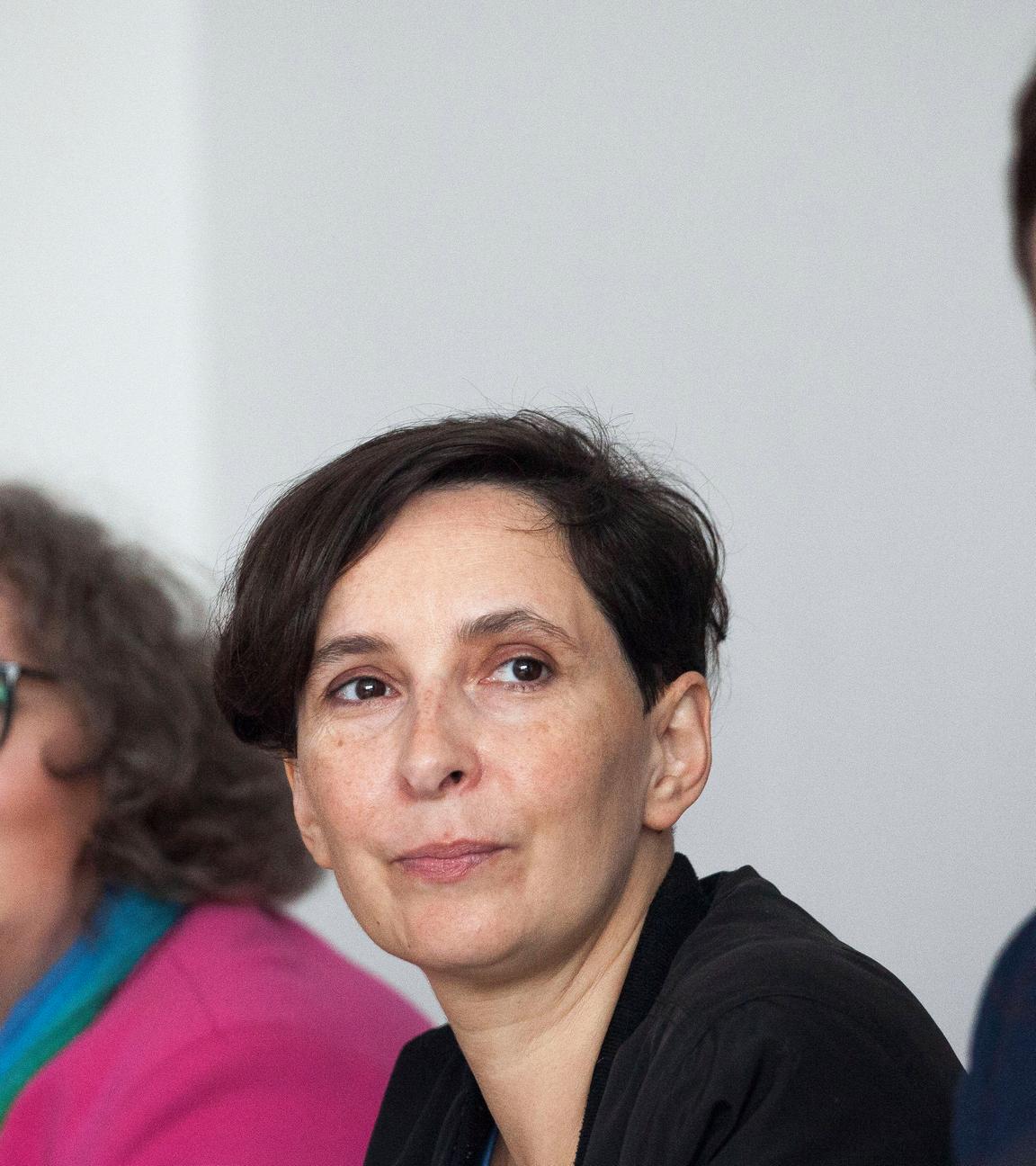 Frau sitzt zwischen zwei Personen u d schaut in die Kamera