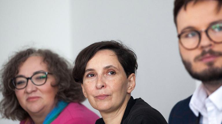 Frau sitzt zwischen zwei Personen u d schaut in die Kamera