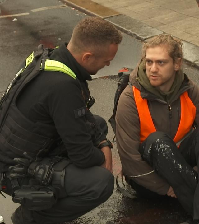 Klima-Aktivist sitzt auf der Straße und diskutiert mit Polizisten