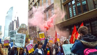 Auf einer Straße in London laufen junge Menschen bei einer Demonstration für das Klima mit Schildern und Pyrotechnik.