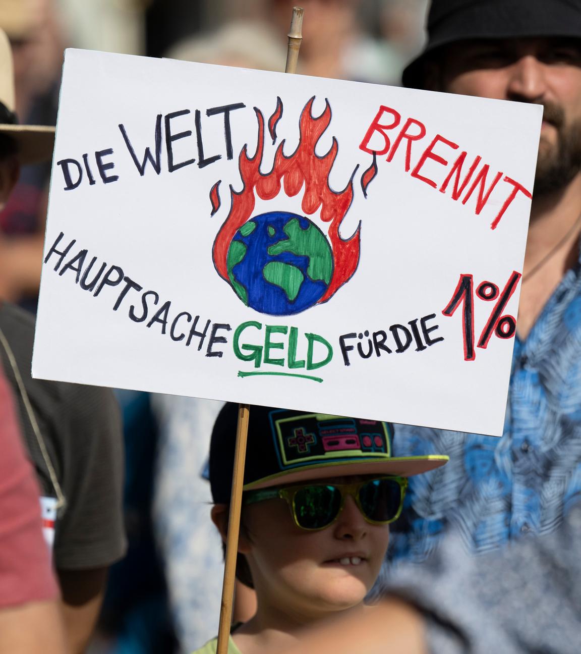 Beim Klimaprotest in Frankfurt hält ein Junge ein Schild hoch: "Die Welt brennt, Hauptsache Geld für die ein Prozent"
