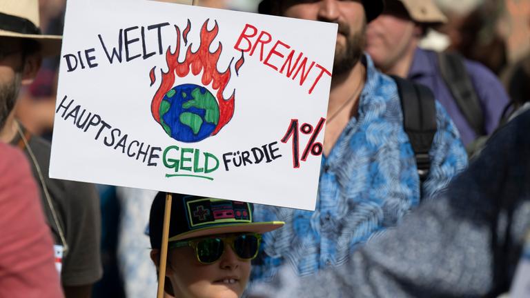 Beim Klimaprotest in Frankfurt hält ein Junge ein Schild hoch: "Die Welt brennt, Hauptsache Geld für die ein Prozent"