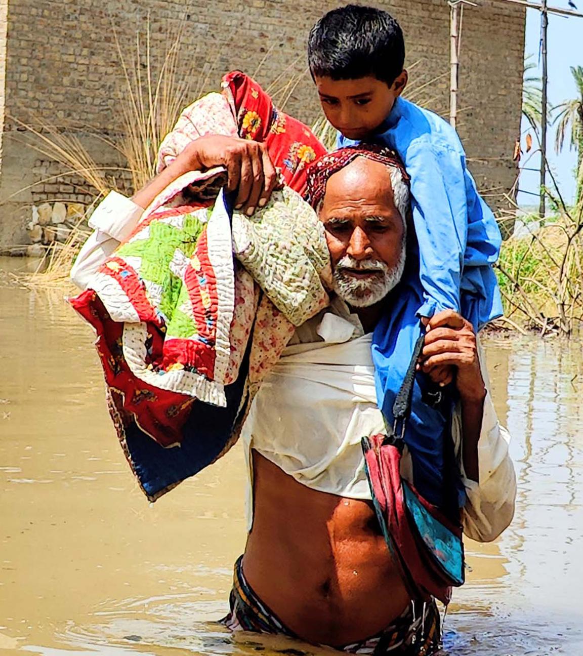 Von der Flut betroffene Menschen waten in Pakistan durch Wasser, um sich in Sicherheit zu bringen.
