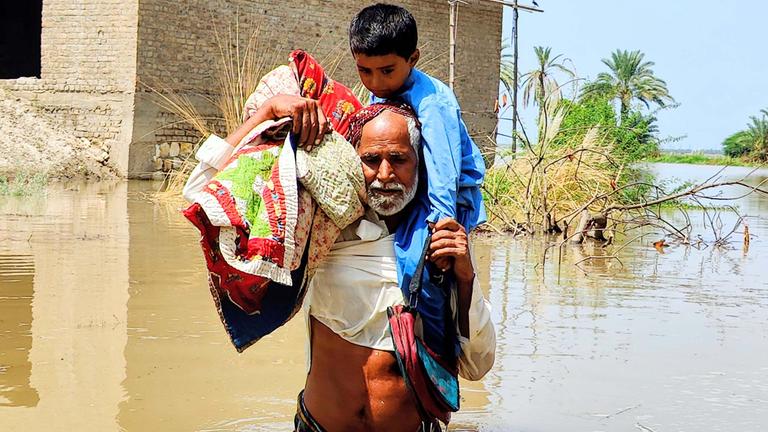 Von der Flut betroffene Menschen waten in Pakistan durch Wasser, um sich in Sicherheit zu bringen.