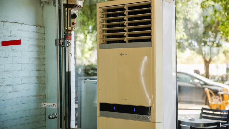 Griechenland, Athen: Eine mobile Klimaanlage steht in einem verglasten Innenraum eines Cafés.