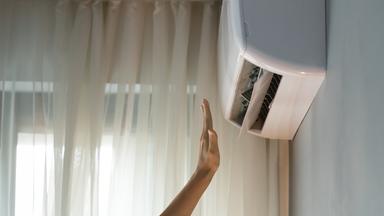 Der Wohnungseigentümer schaltet die Klimaanlage ein, überprüft das Bedienelement und streckt die Hand in den Luftstrom.