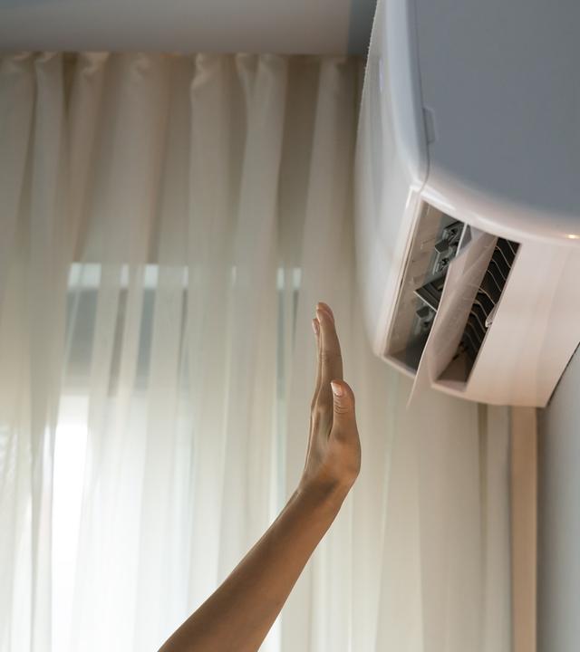 Der Wohnungseigentümer schaltet die Klimaanlage ein, überprüft das Bedienelement und streckt die Hand in den Luftstrom.