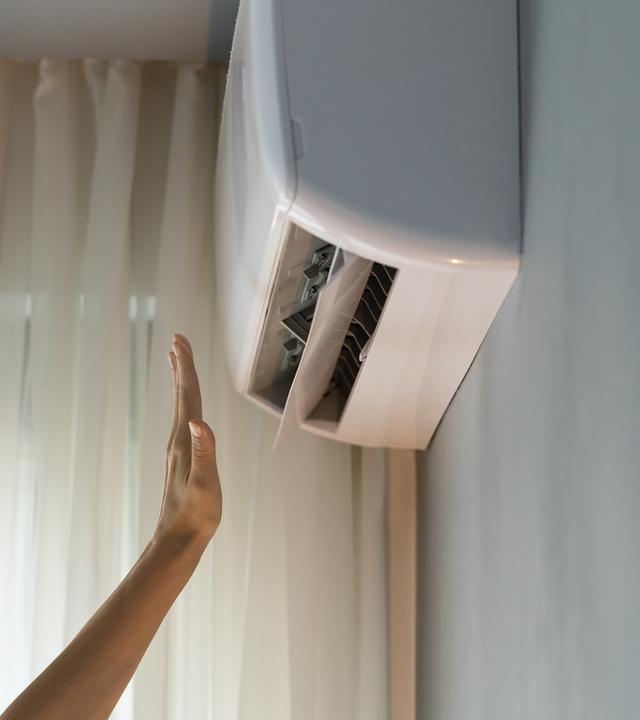 Eine fest installierte Klimaanlage in einer Wohnung wird getestet, indem eine Hand in den Luftstrom gehalten wird. 