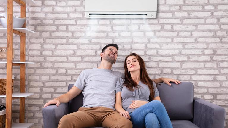 Junges Paar sitzt auf der Couch, dahinter eine Klimaanlage
