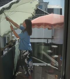 Eine Frau positioniert einen Sonnenschirm auf einen Balkon.