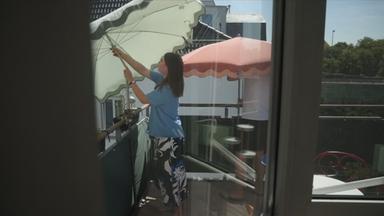 Eine Frau positioniert einen Sonnenschirm auf einen Balkon.