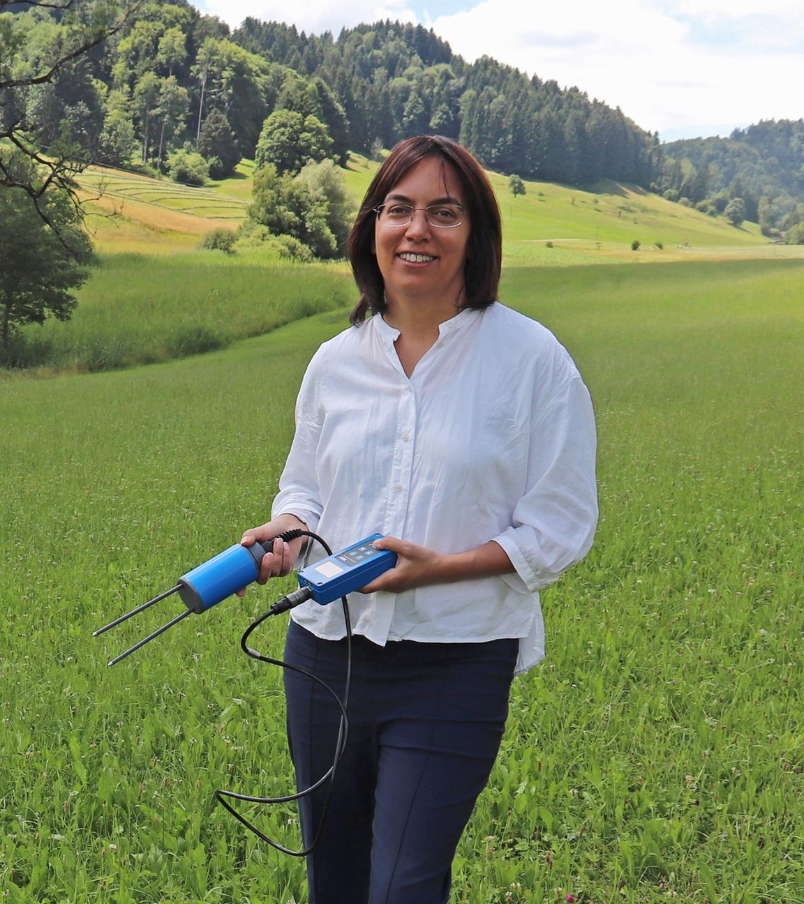Die Schweizer Klimaforscherin Sonia Isabelle Seneviratne steht mit einem Bodenfeuchtemessgerät auf einer Wiese im Schweizer Voralpenland